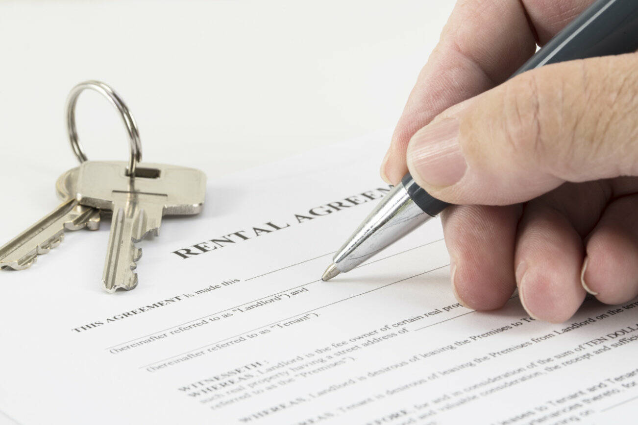 hand is writing with a pen on a rental agreement document, house keys in the background, selected focus, narrow depth of field