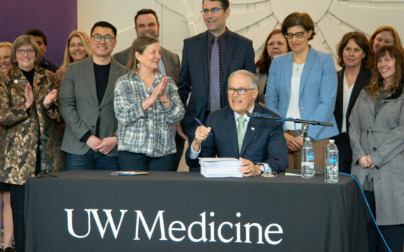 Washington Gov. Jay Inslee (seated) prepares to sign the 2024 supplemental budget on March 29, 2024. He was joined by several Democratic state lawmakers, including, to his right, Sen. June Robinson, the lead Senate budget writer. (Courtesy of UW Medicine | Nicholas Swatz)