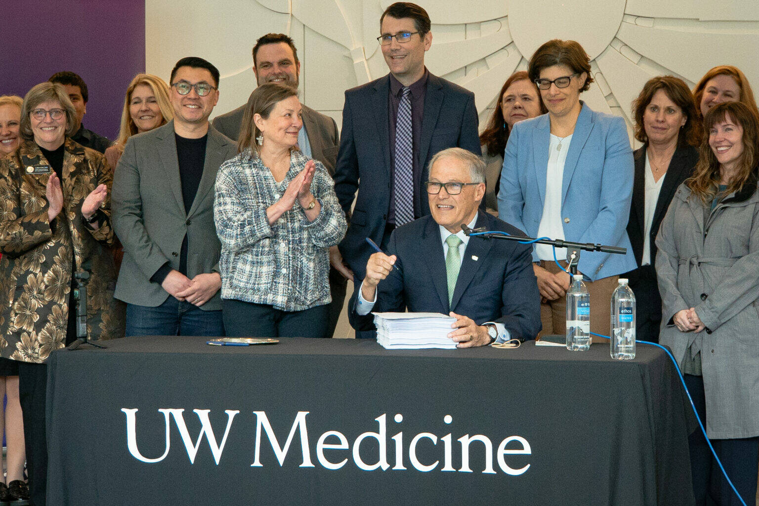 Washington Gov. Jay Inslee (seated) prepares to sign the 2024 supplemental budget on March 29, 2024. He was joined by several Democratic state lawmakers, including, to his right, Sen. June Robinson, the lead Senate budget writer. (Courtesy of UW Medicine | Nicholas Swatz)